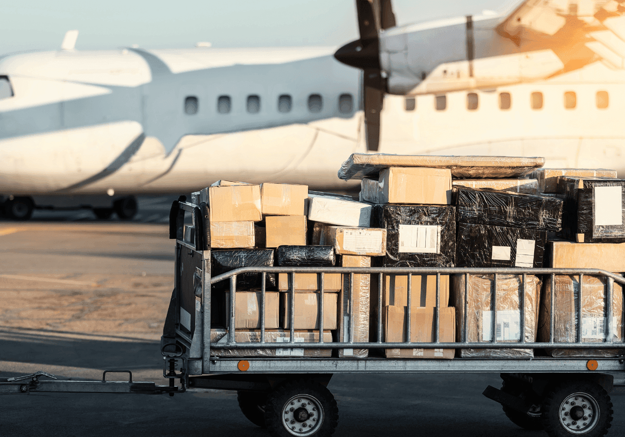 A cargo cart loaded with packages in front of a white airplane on an airport tarmac.