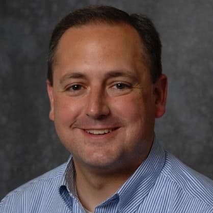 Smiling man with short brown hair and a blue striped collared shirt.