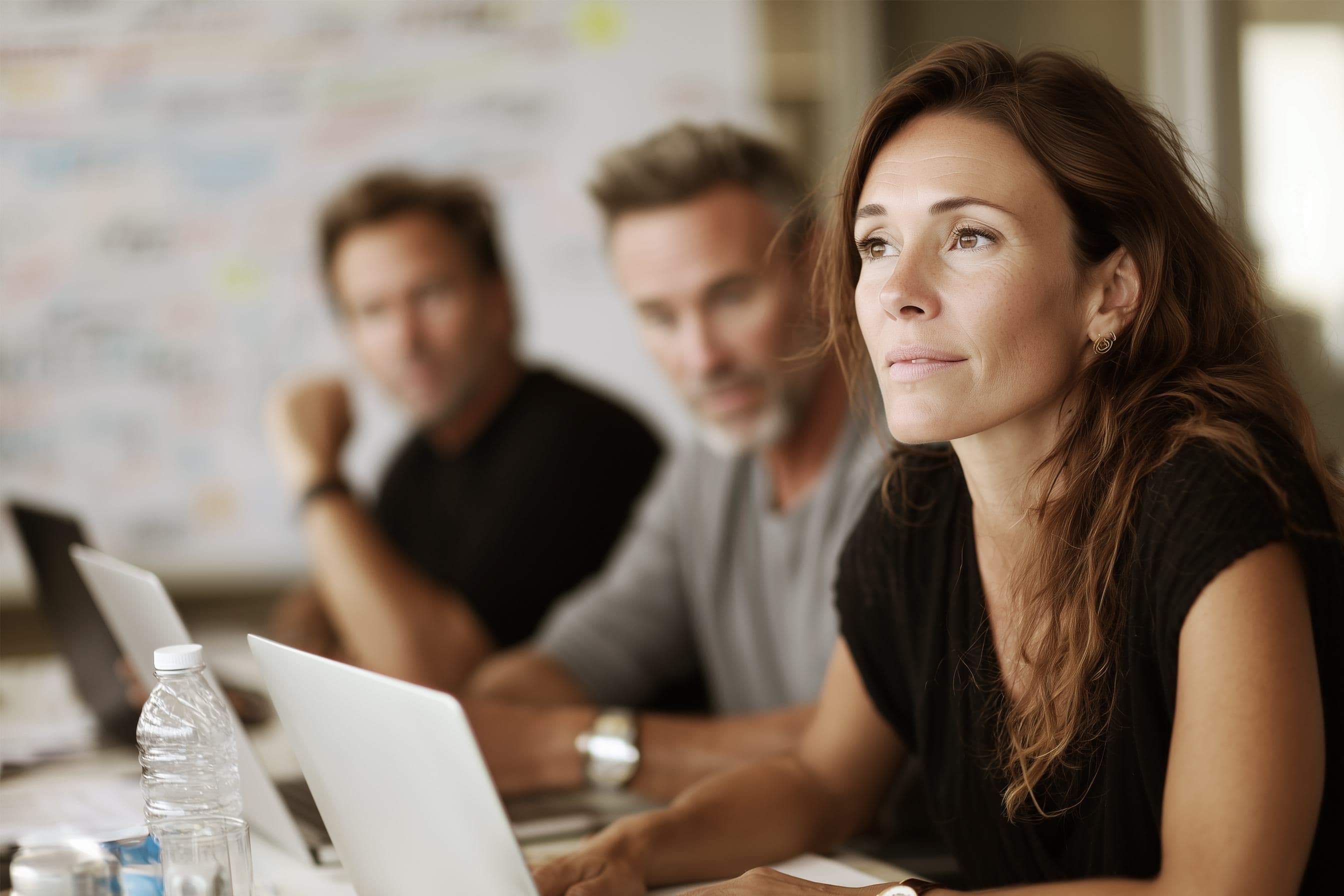 Thoughtful woman in a dark top attending a business meeting with two colleagues.